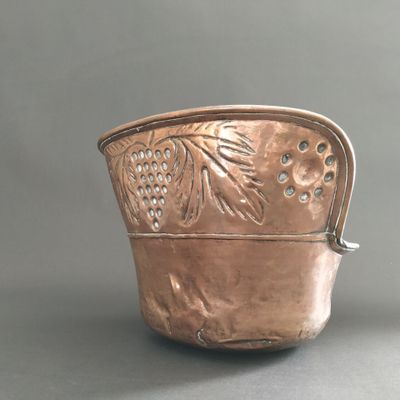 a silver pot with grapes on it sitting on a table