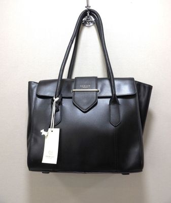 un sac à main en cuir noir accroché à un mur, avec une étiquette attachée dessus
