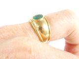 a man ' s hand holding a gold ring with a green stone on it