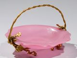 a pink bowl with a gold handle on a white surface