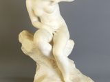 une statue en marbre blanc représentant un garçon assis sur un rocher