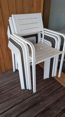 plusieurs chaises en plastique blanc posées sur une terrasse en bois, près d'une porte vitrée