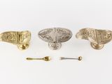 three antique brass drawer pulls and a spoon on a white surface