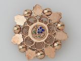 une image représentant une broche en or ornée d'une fleur bleue au centre
