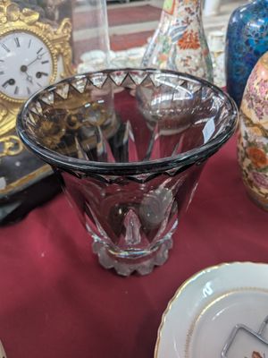a glass vase sitting on a table with a clock in the background
