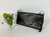 a black leather purse next to a vase with purple flowers