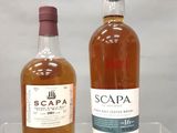 Deux bouteilles de Scappa et une bouteille de vin sont posées sur une étagère transparente.