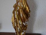 a gold statue on a wooden table with a white wall behind it