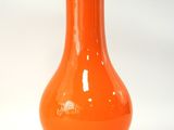 un vase orange posé sur une surface blanche