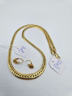 un collier et une paire de boucles d'oreilles en or posés sur une surface blanche