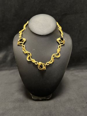 a gold plated necklace on a mannequin with a black background