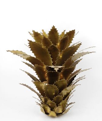 a close up of a metal pineapple plant on a white surface