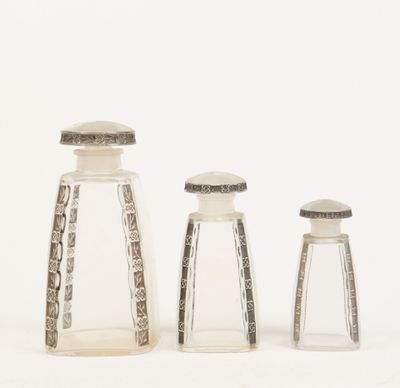 three clear glass bottles with silver trims and lids on a white surface