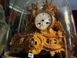 une horloge en or posée sur une table, sous une cloche en verre