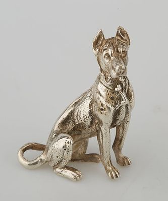 an antique silver dog figurine sitting on a white surface