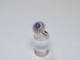 une photo d'une bague sertie d'un saphir bleu et de diamants, posée sur une surface blanche