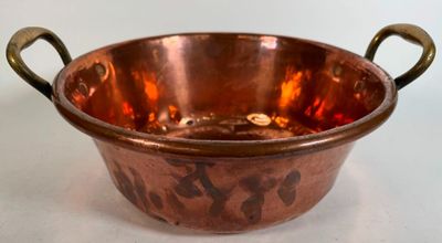 an old copper bowl with handles on a white surface