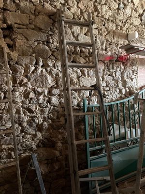 Plusieurs échelles sont appuyées contre un mur de pierre dans une pièce.