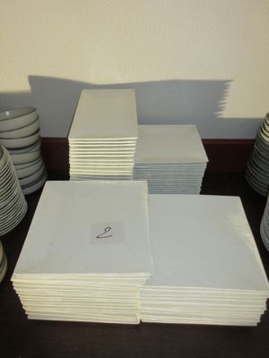 plusieurs piles d'assiettes et de tasses blanches posées sur une table, avec un mur en arrière-plan