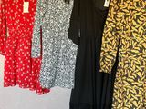 trois robes suspendues à un portant dans une pièce où se trouvent des vêtements sur des cintres