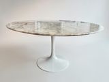 une table à manger ovale en marbre, avec un piètement blanc et un plateau en verre