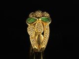 a close up of a gold ring with green stones on a black surface