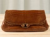 crocodile skin purse on a wooden table with a curtain in the background