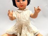a small doll sitting on the ground with a leaf