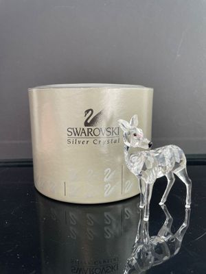 une figurine de cerf en verre posée sur une table, à côté d'une bougie