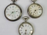 three antique pocket watches sitting on top of a white surface