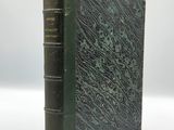 an old book with a green cover sitting on a white surface