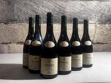 six bottles of wine are lined up on a table in front of a brick wall