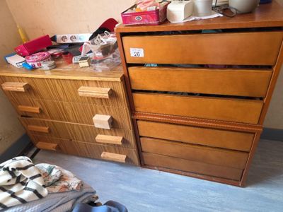 une commode et un lit dans une chambre où le sol est encombré d'objets