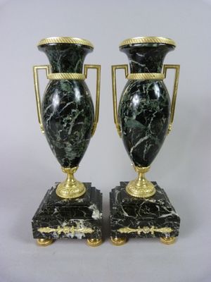 paire de vases noirs et dorés munis d'anses, posés sur des socles en marbre