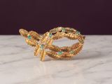 a close up of a gold ring with green stones on a marble surface