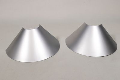 deux cônes métalliques posés sur une surface blanche, avec une lumière en arrière-plan