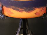 purple and orange bowl with flowers on a stand against a black background