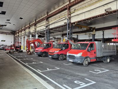 Plusieurs camions rouges sont garés dans un grand entrepôt, où se trouve un homme sur une nacelle élévatrice.