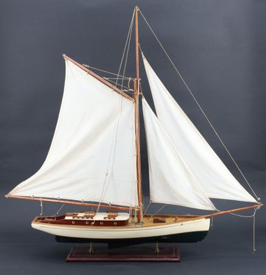maquette en bois d'un voilier aux voiles blanches, posée sur un socle