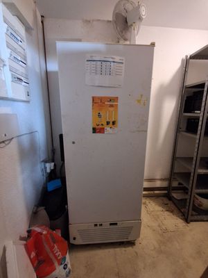 un réfrigérateur dans un coin d'une pièce, avec un ventilateur posé dessus