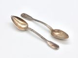 two silver spoons sitting on top of each other on a white surface