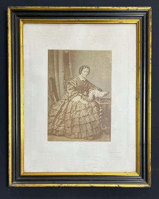 une vieille photo représentant une femme en robe, assise sur une chaise