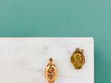 un gros plan sur une paire de boucles d'oreilles en or posées sur une surface en marbre