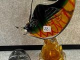 une sculpture en verre représentant un poisson, posée sur un socle à côté d'autres objets en verre