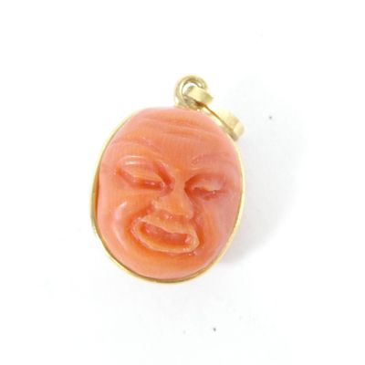 une photo d'un pendentif en forme de visage de couleur corail, monté sur une chaîne plaquée or