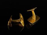 two gold cufflinks on a black surface with a black background