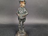 une vieille statue en bronze représentant un homme coiffé d'un haut-de-forme et muni d'une canne