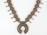 a necklace made of silver and copper beads with a horseshoe pendant