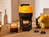une cafetière posée sur une table, à côté d'un bol de fruits et d'une tasse de café