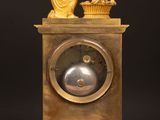 a gold clock sitting on a wooden table with a statue on top of it